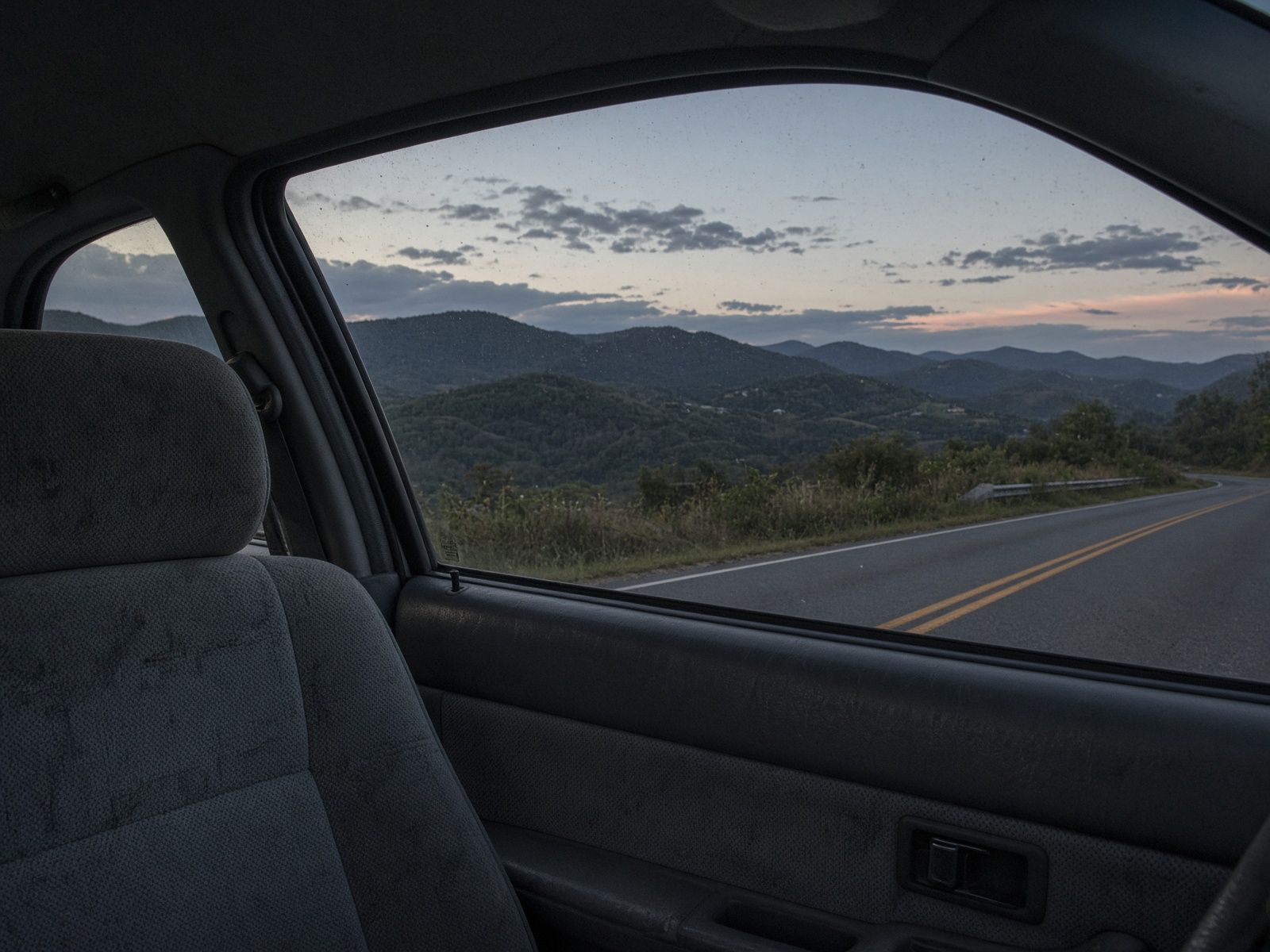 View from a passenger seat looking out at rolling hills at dusk